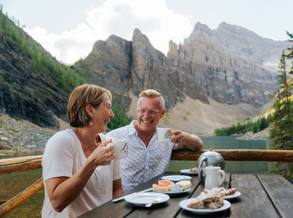 A couple sits at a picnic table at the Lake Agnes Tea House after hiking in Banff National Park.