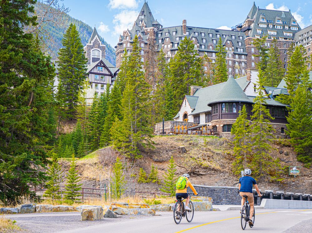 Two people bike in Banff on the access point to the Spray River Loop in Banff National Park.