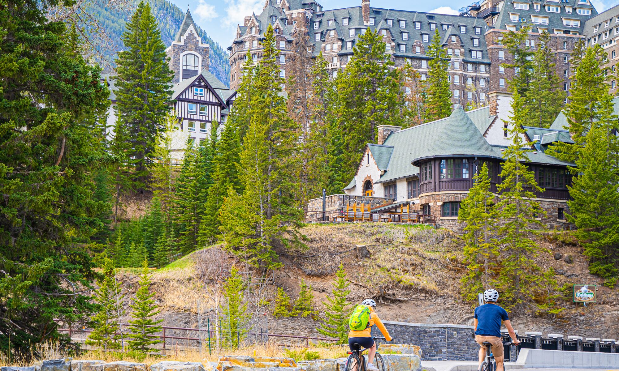 Two people bike in Banff on the access point to the Spray River Loop in Banff National Park.