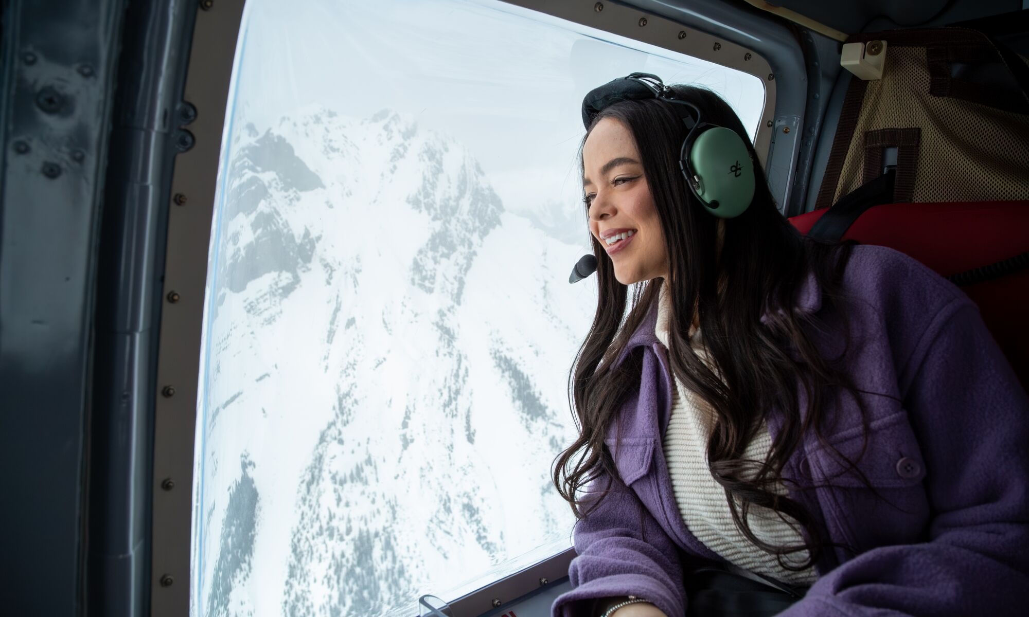 A girl in a helicopter looking out onto the snowy mountains in Banff National Park