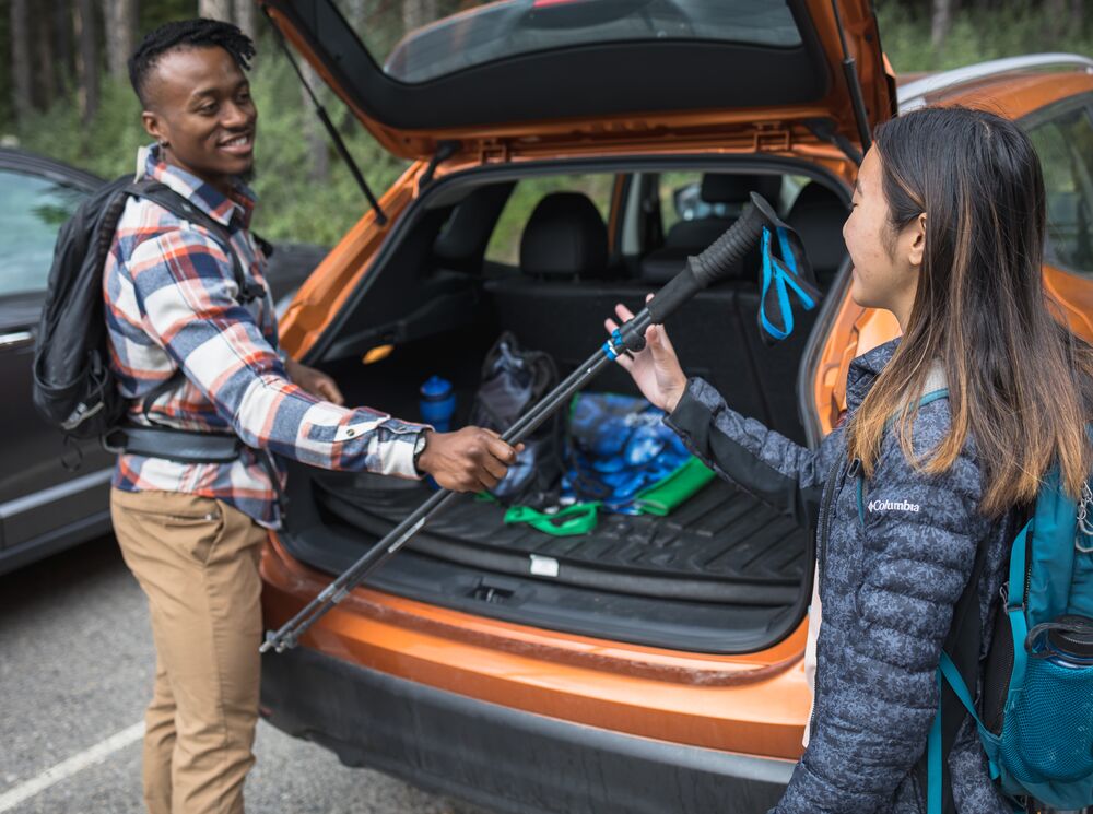 A person hands a hiking pole to another person from a vehicle while they get ready for hiking at Lake Minnewanka in Banff National Park.