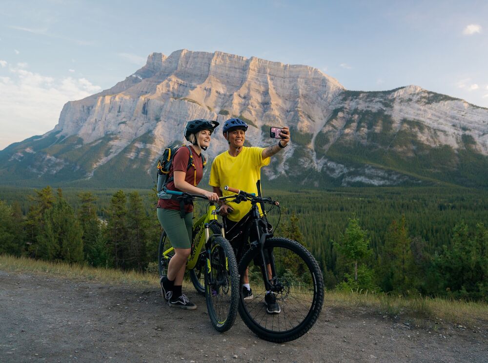 Two people take a photo while mountain biking in Banff at the Tunnel Mountain Trail.
