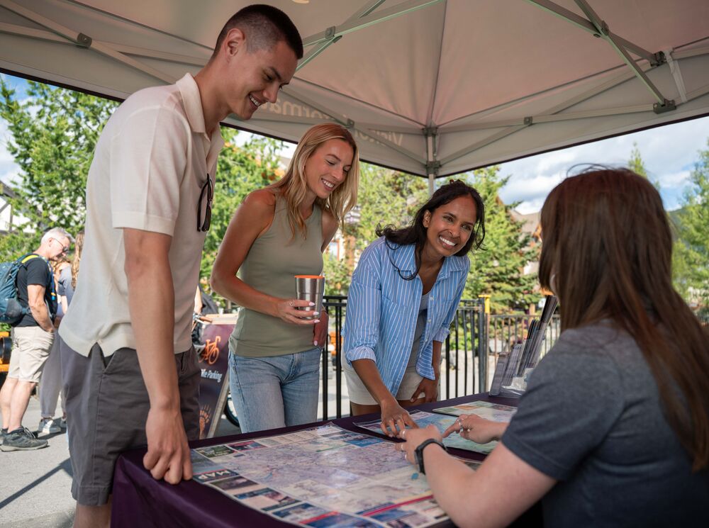 Three people looking at a map and getting information from a person on Banff Ave in Banff National Park