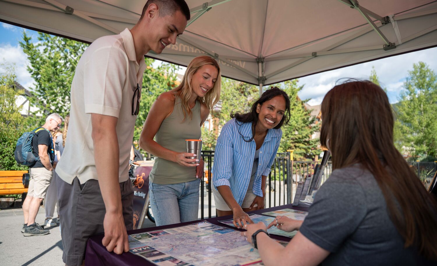Three people looking at a map and getting information from a person on Banff Ave in Banff National Park