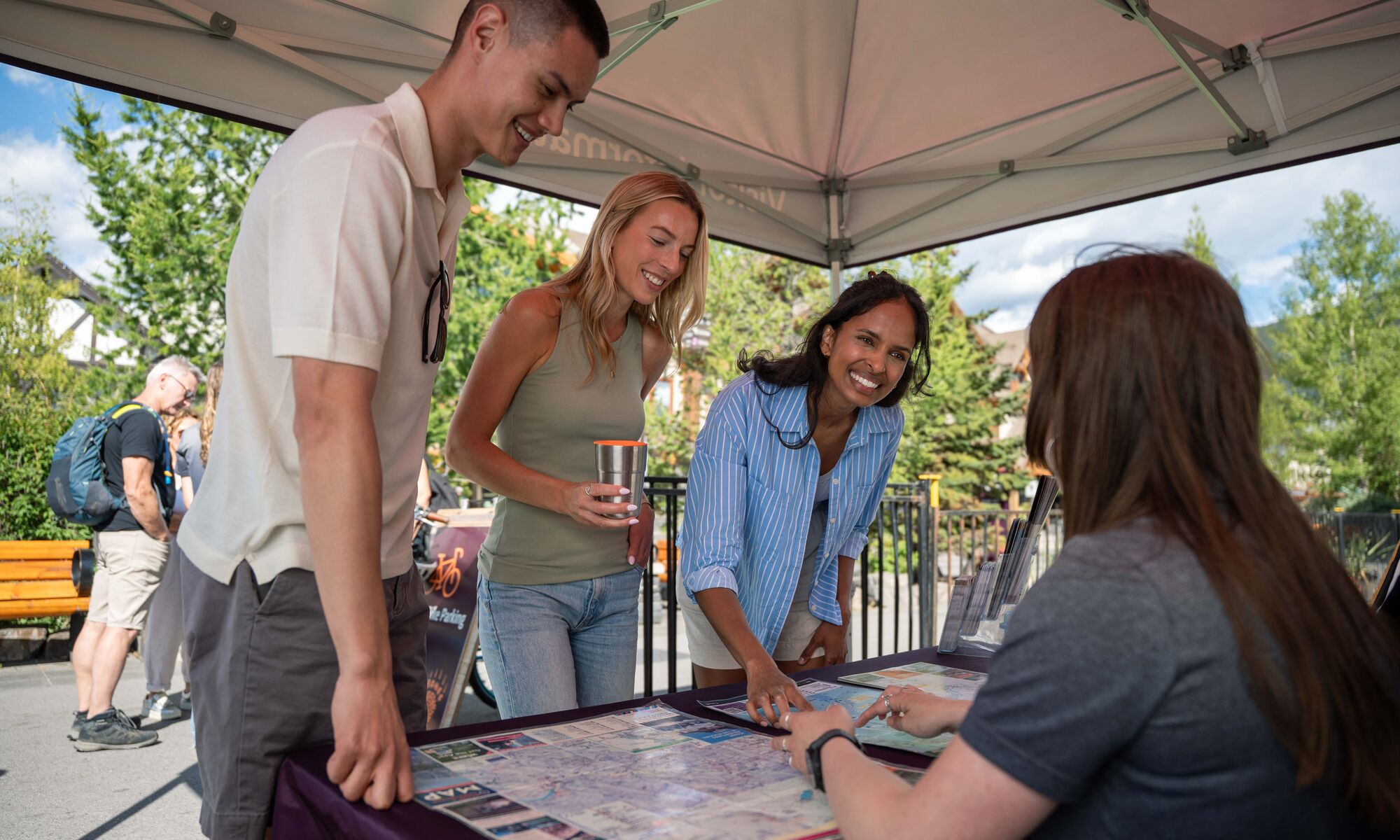 Three people looking at a map and getting information from a person on Banff Ave in Banff National Park