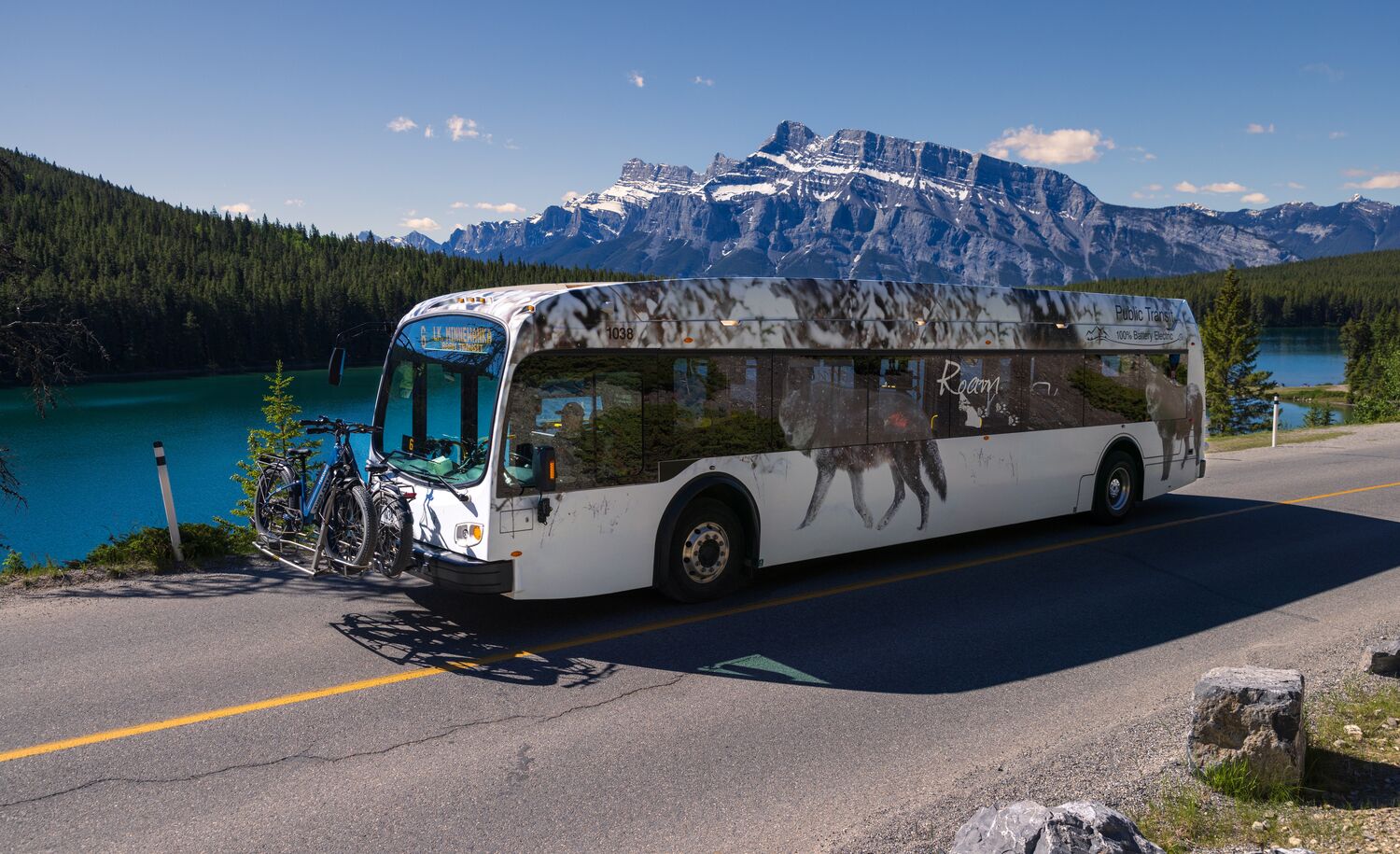A Roam Transit bus drives the Minnewanka Loop in Banff National Park on a blue bird day in front of Two JAck Lake.