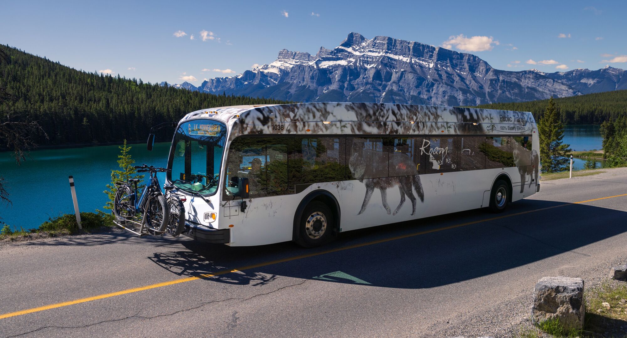 A Roam Transit bus drives the Minnewanka Loop in Banff National Park on a blue bird day in front of Two JAck Lake.