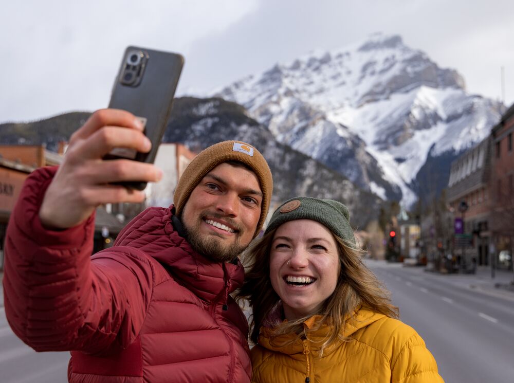 A couple taking a selfie on Banff Avenue with Cascade in the back in Banff National Park