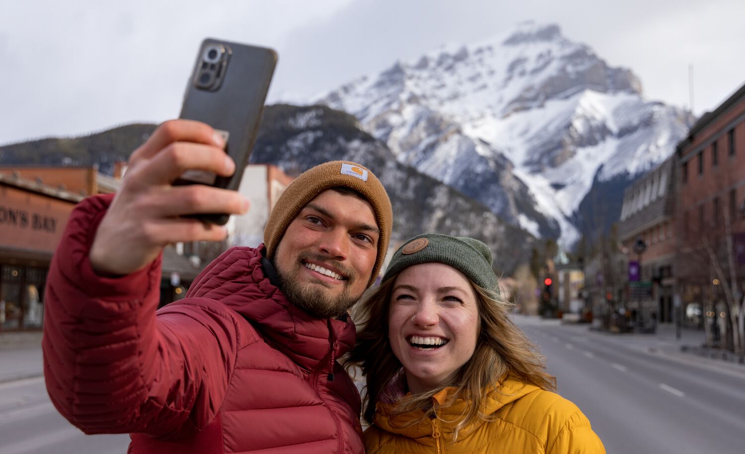A couple taking a selfie on Banff Avenue with Cascade in the back in Banff National Park