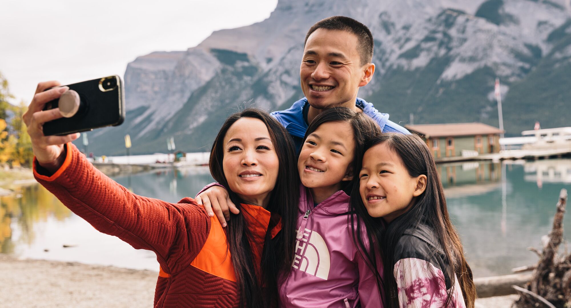 A family of four takes a photo on the shores of Lake Minnewanka during a hike on a fall day in Banff National Park.