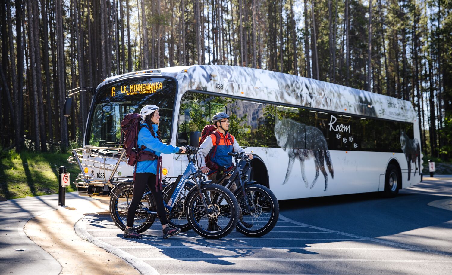 Two people walk away from a Roam Transit bus with their bikes, heading out for a bike ride in Banff National Park.