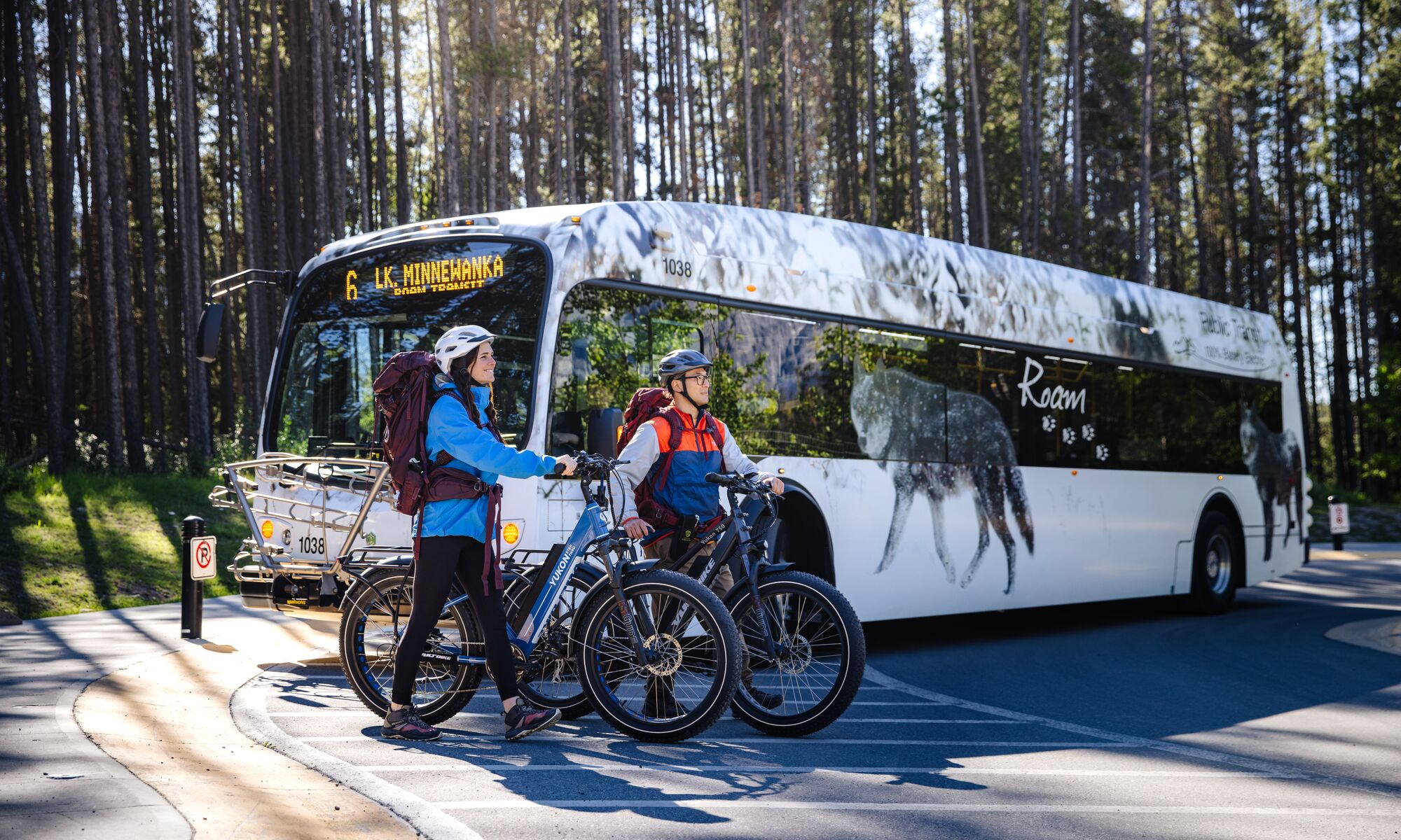 Two people walk away from a Roam Transit bus with their bikes, heading out for a bike ride in Banff National Park.