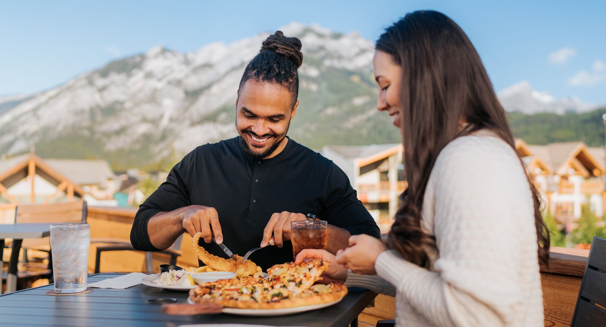 A couple enjoys food and drinks on the Rose & Crown patio in Banff on a hot summer day.