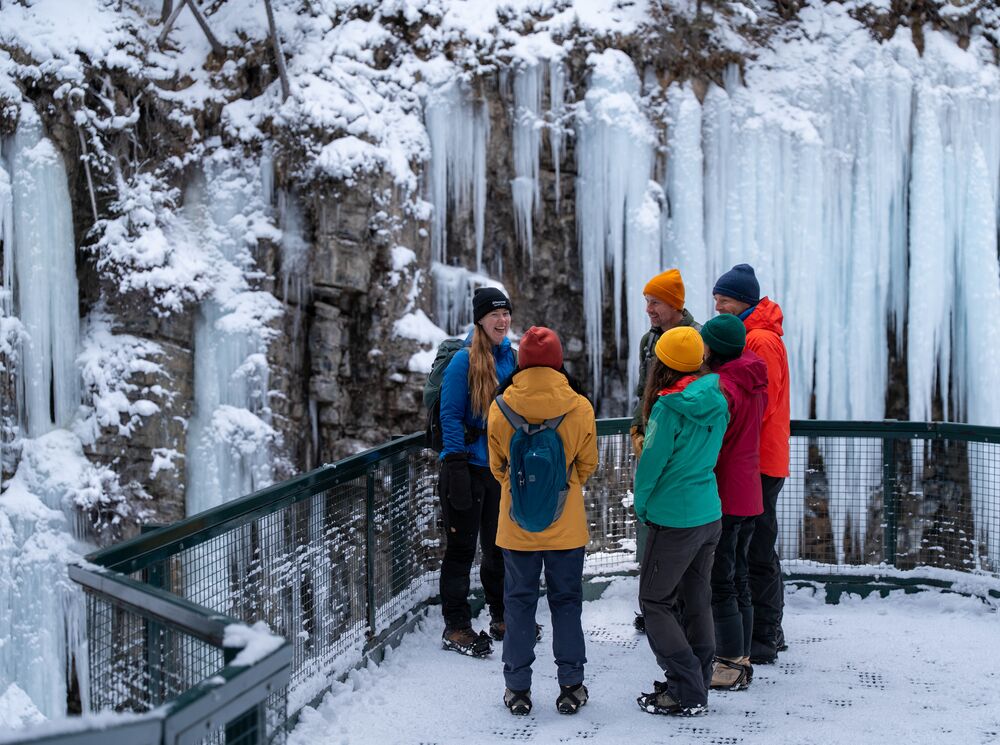 A group of people on a guided tour stand at the Upper Falls after hiking in Banff National Park in the winter at Johnston Canyon.