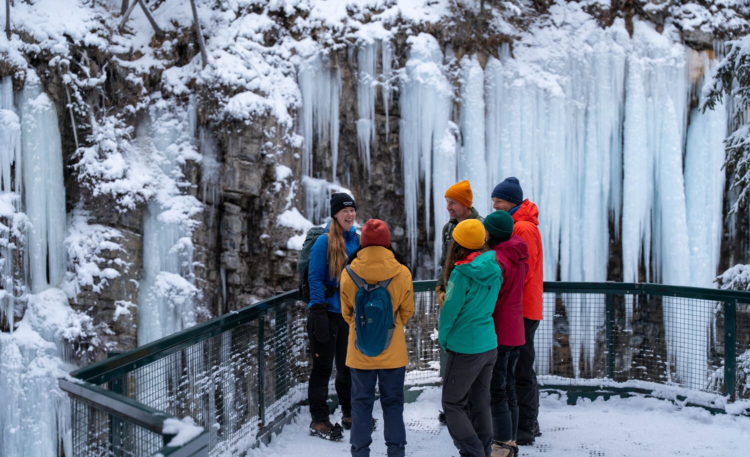 A group of people on a guided tour stand at the Upper Falls after hiking in Banff National Park in the winter at Johnston Canyon.