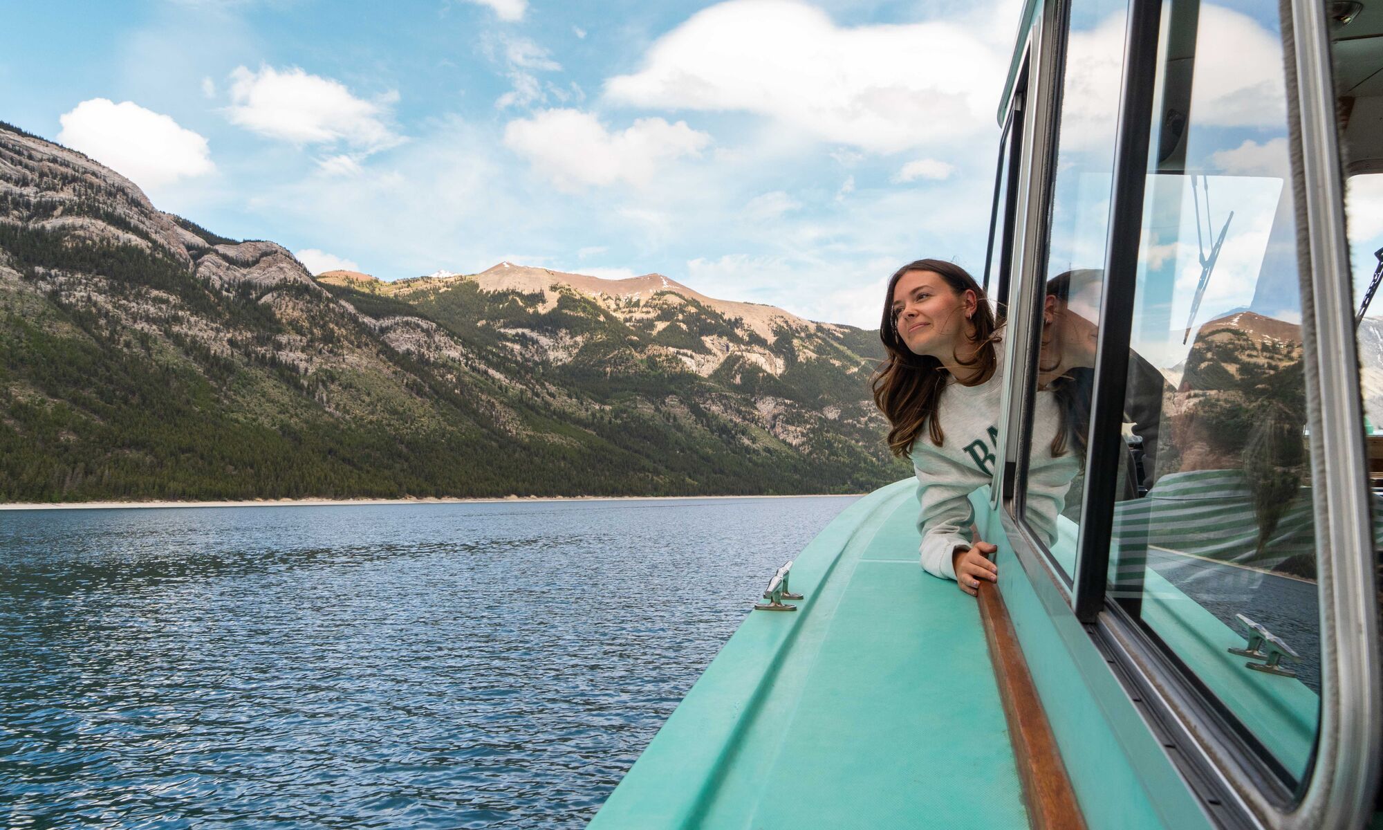 A women on The Lake Minnewanka Cruise out on Lake Minnewanka in Banff National Park with a mountain in the background.