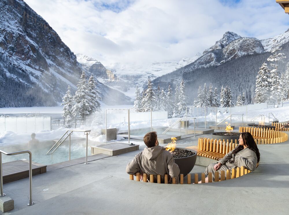 A couple sitting at an outdoor fire at the Fairmont Basin Glacier Waters spa in Lake Louise