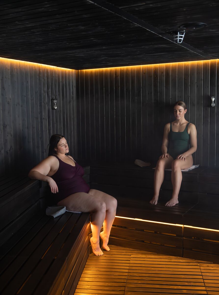 Two women sit in a sauna with mood lighting at the BASIN Glacier Waters Spa in Lake Louise, a popular thing to do in August in Banff National Park
