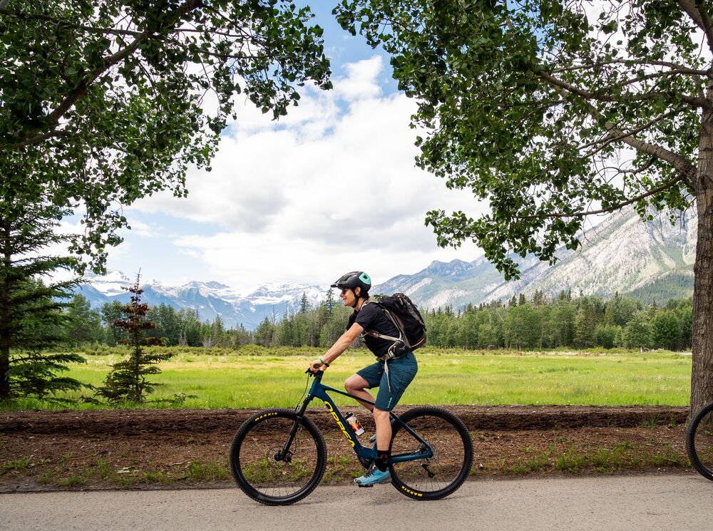 Two people bike along a road in Banff National Park, heading towards the Sundance Trail on a bike tour.