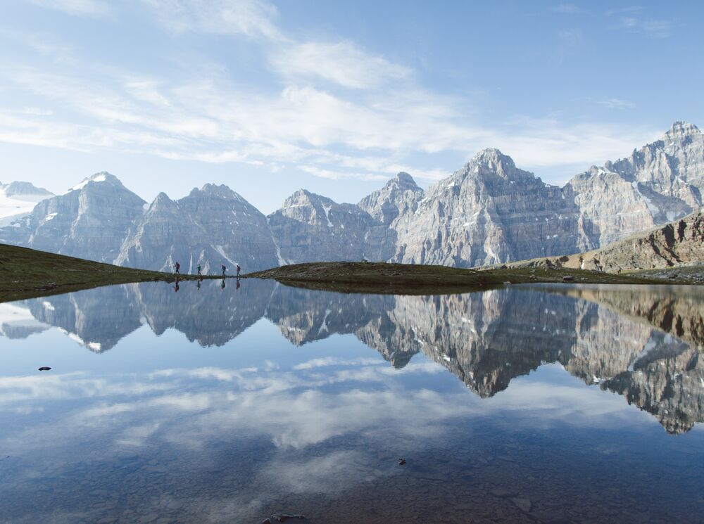 Four people reflected in a lake in Larch Valley with the mountains of the Valley of the Ten Peaks behind them while taking a hike at Moraine Lake in Banff National Park.