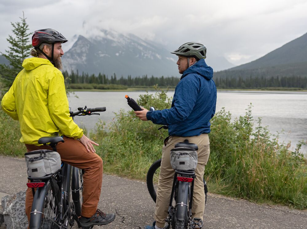 A person hands a bear spray to another person while biking in Banff National Park near Vermilion Lakes.