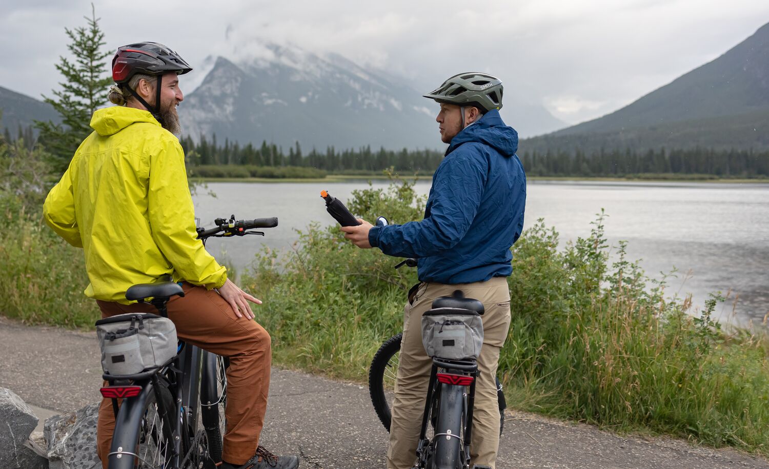 A person hands a bear spray to another person while biking in Banff National Park near Vermilion Lakes.