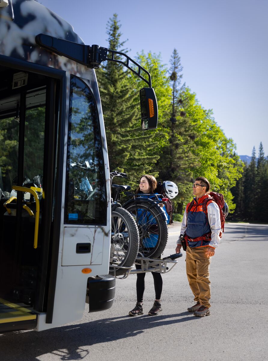 Two people get their bikes off the bike rack on a Roam Transit bus in Banff National Park.
