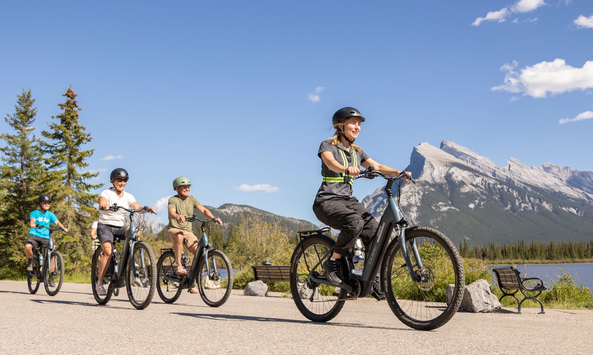 A group of people ride e-bikes in Banff National Park on Vermilion Lakes Road on a bluebird day with Mount Rundle in the background.