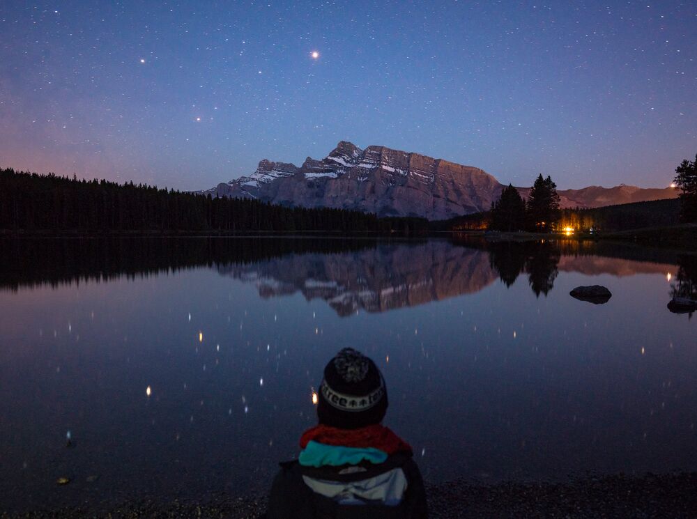 Person sitting at Two Jack Lake at night in Banff National Park
