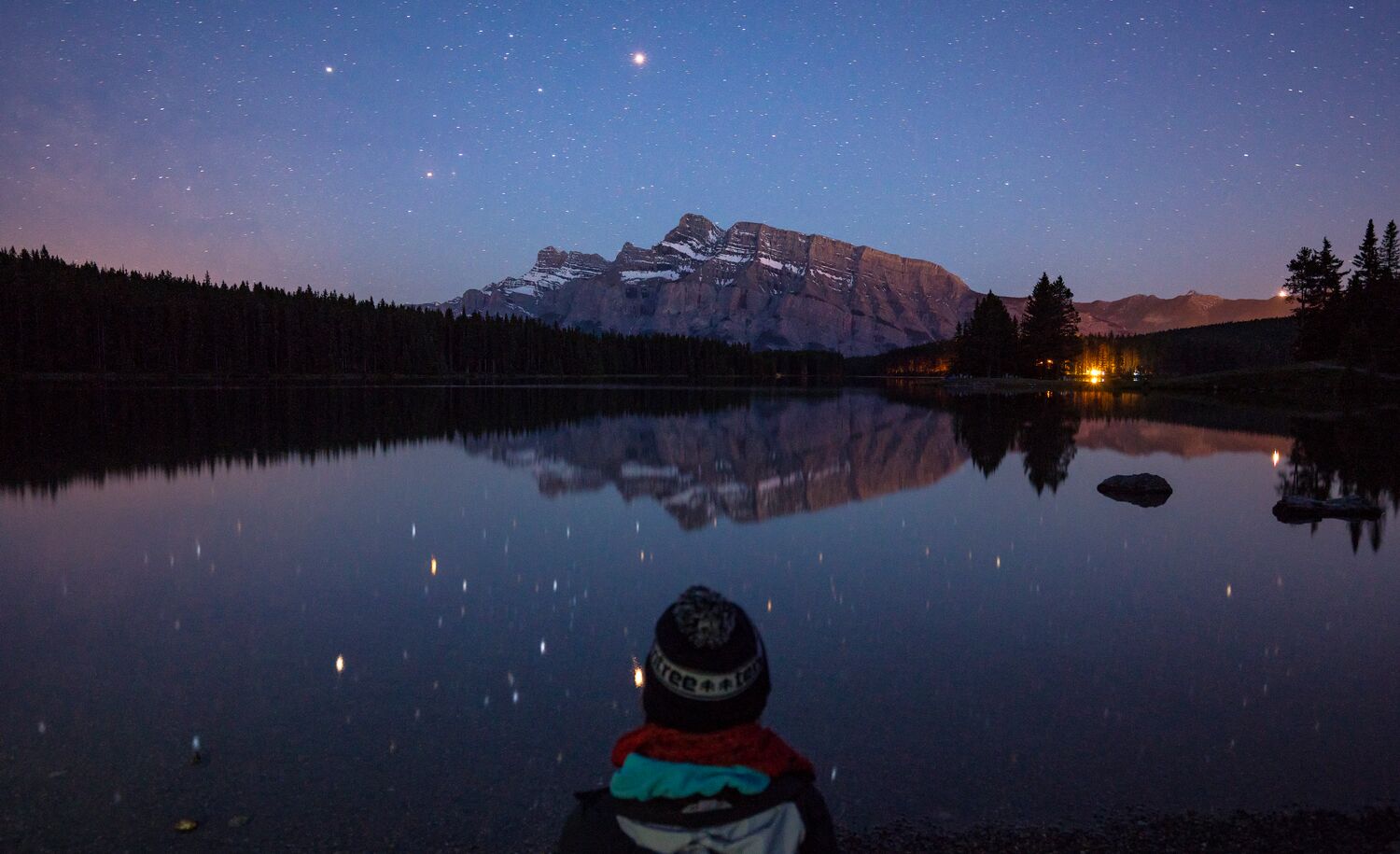 Person sitting at Two Jack Lake at night in Banff National Park