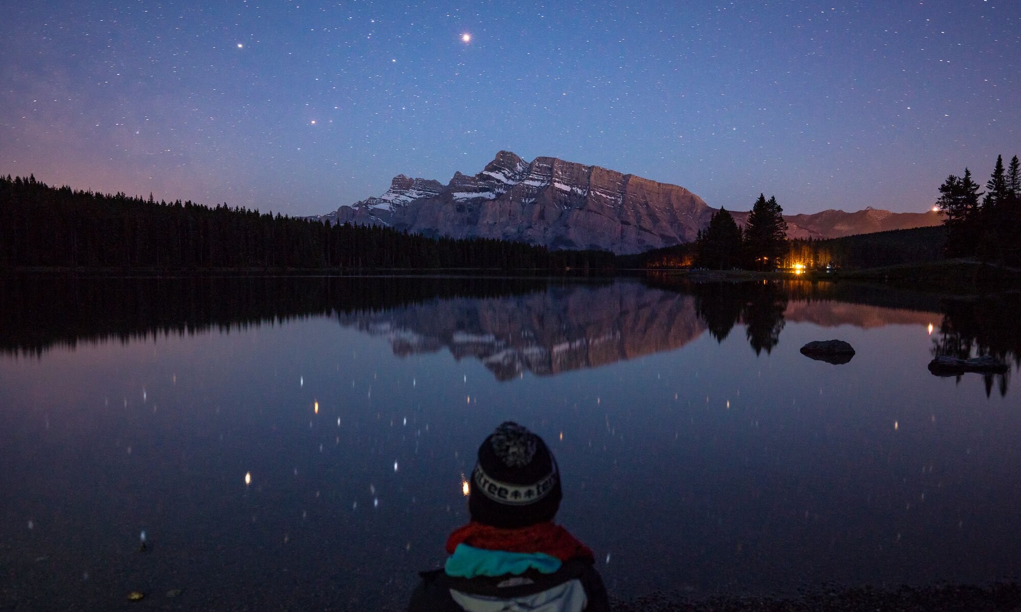 Person sitting at Two Jack Lake at night in Banff National Park