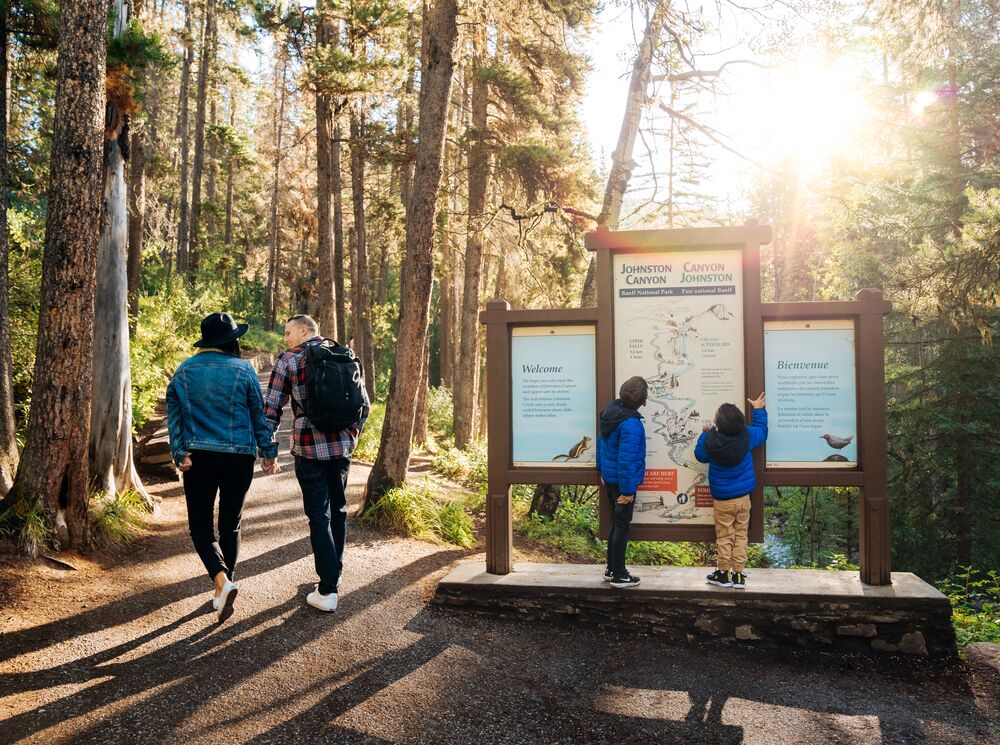 A family looks at a trail sign at Johnston Canyon in Banff National Park at the start of a hike in the summer.