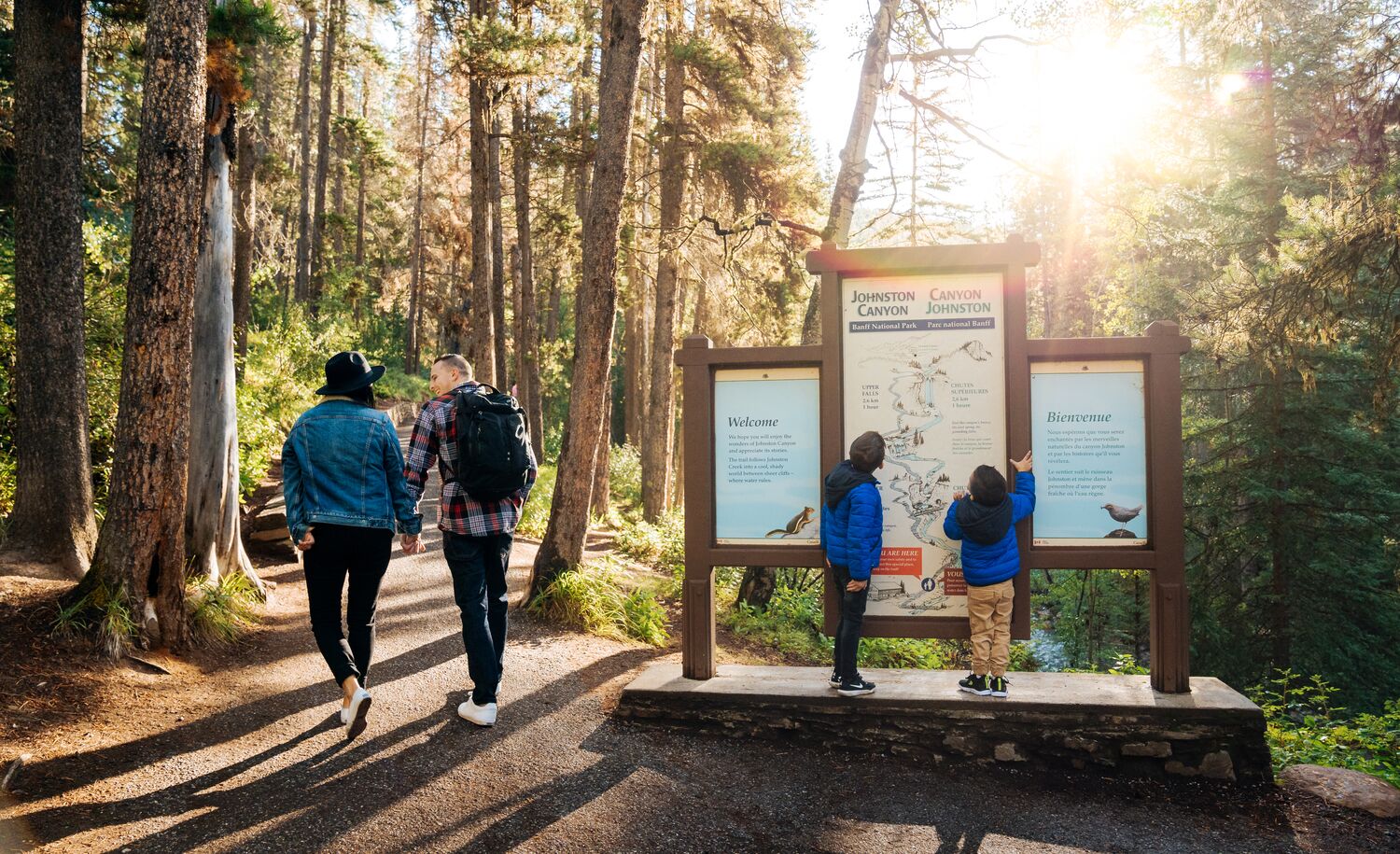 A family looks at a trail sign at Johnston Canyon in Banff National Park at the start of a hike in the summer.