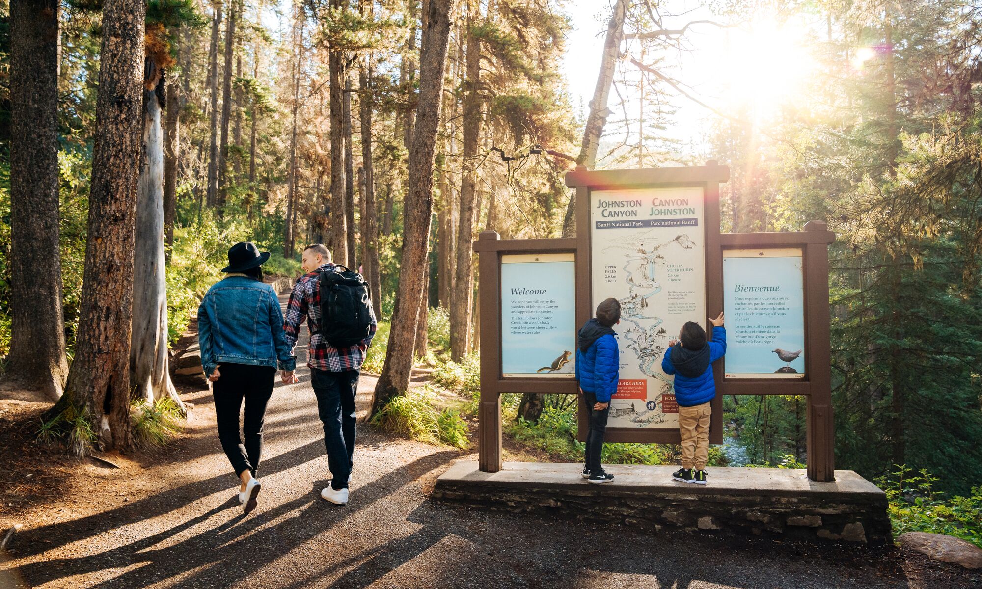 A family looks at a trail sign at Johnston Canyon in Banff National Park at the start of a hike in the summer.