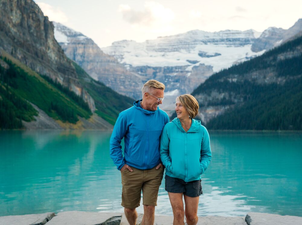 Two people walk at the Lake Louise lakeshore in Banff National Park at sunset.