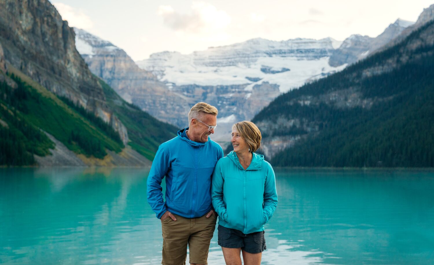 Two people walk at the Lake Louise lakeshore in Banff National Park at sunset.