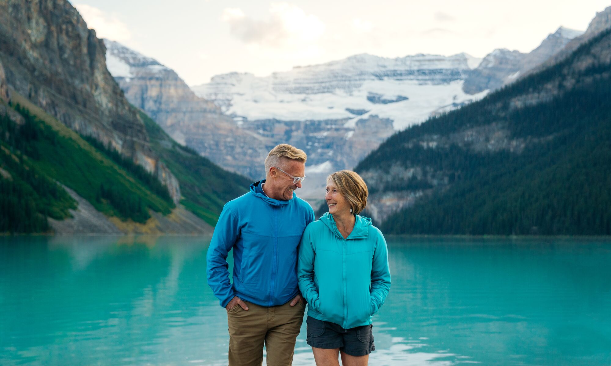 Two people walk at the Lake Louise lakeshore in Banff National Park at sunset.