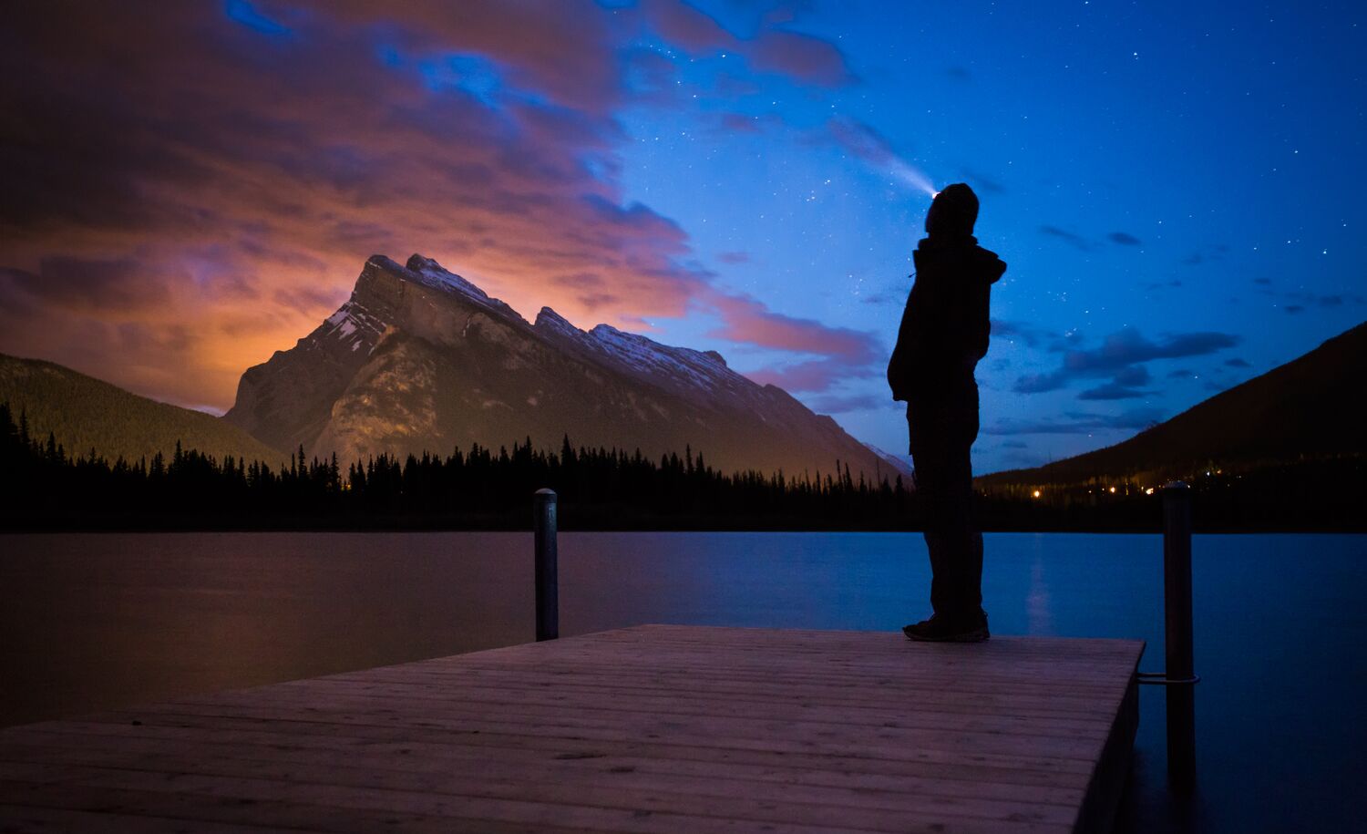 A person standing on a dock looking at the northern lights in Banff National Park