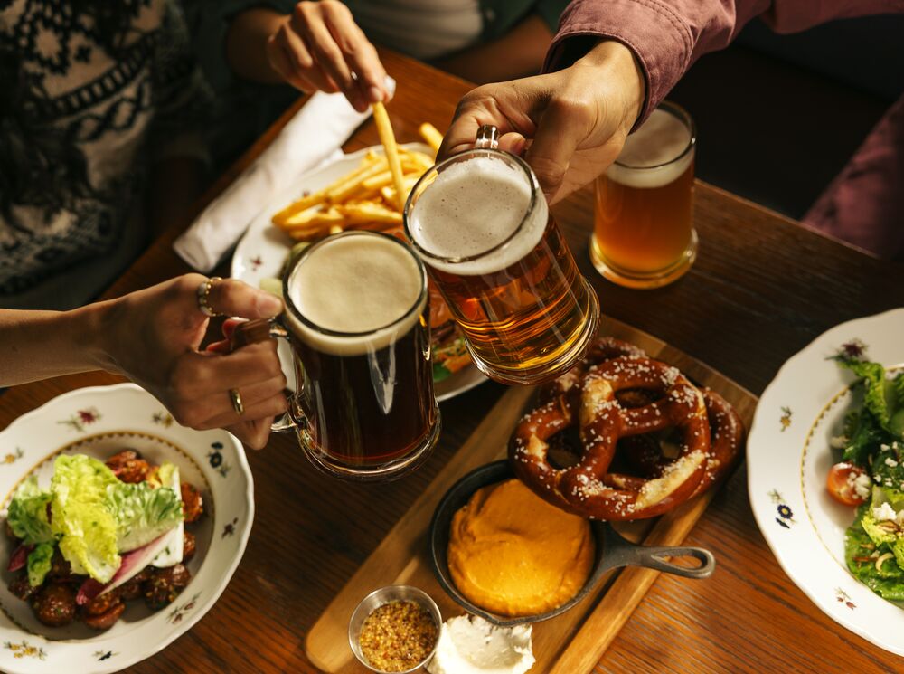 A table features beer and plated food including warm pretzels, fries, and appetizers