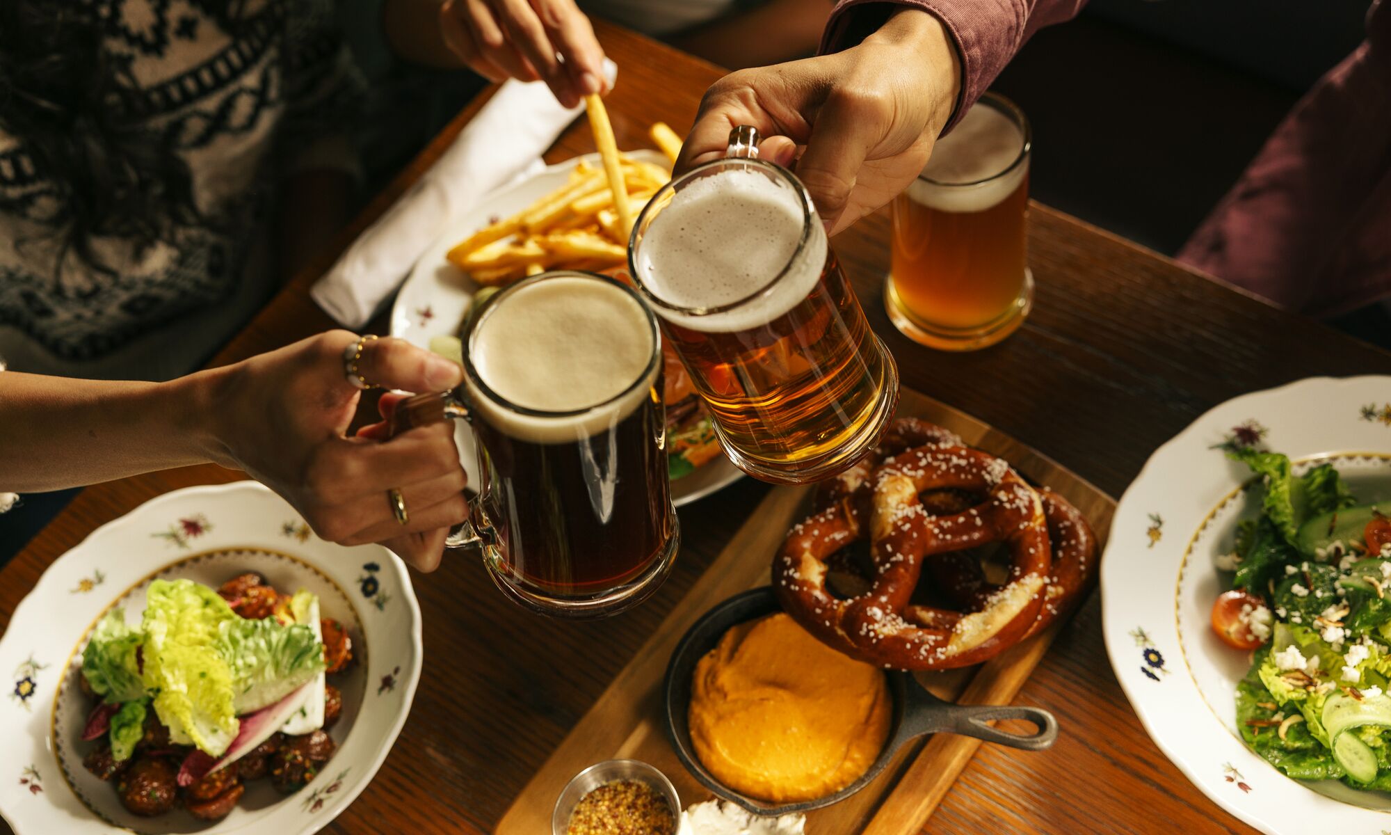 A table features beer and plated food including warm pretzels, fries, and appetizers