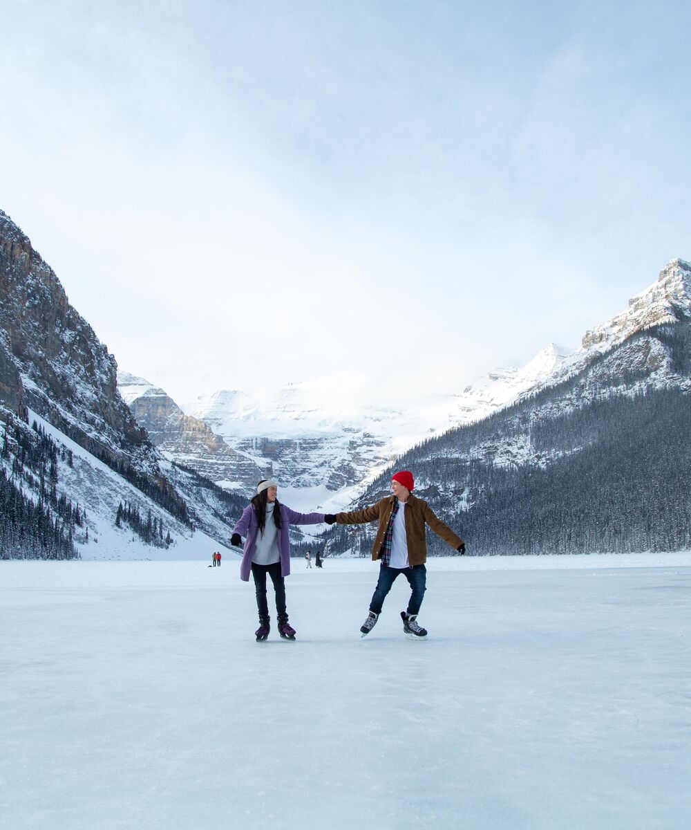 Two people skating on the ice rink on Lake Louise with the Victoria Glacier in the background