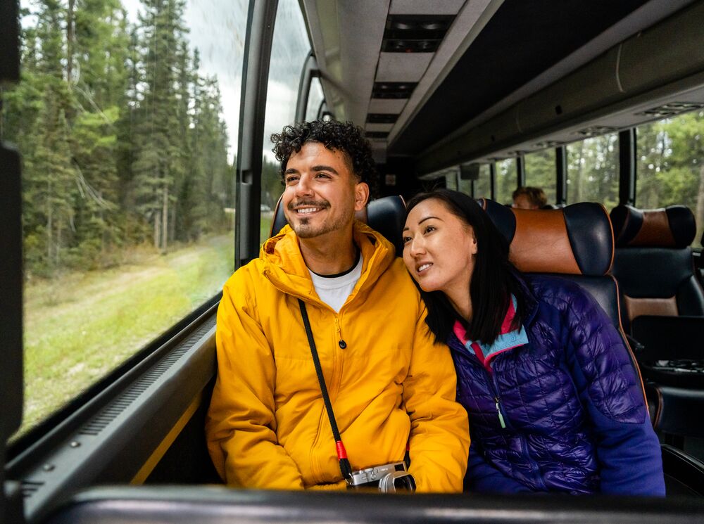 Two people look out the window on a Parks Canada shuttle to Moraine Lake.