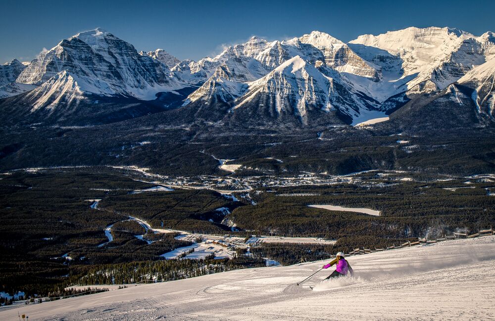 A person enjoys downhill skiing at the Lake Louise Ski Resort in Banff National Park on a clear blue day