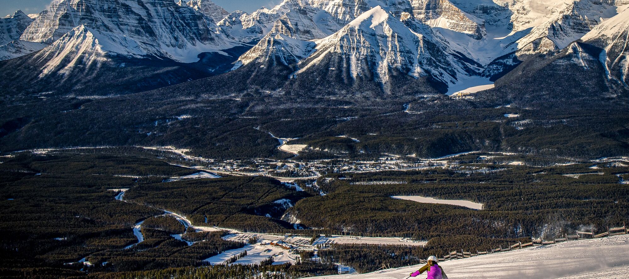 A person enjoys downhill skiing at the Lake Louise Ski Resort in Banff National Park on a clear blue day