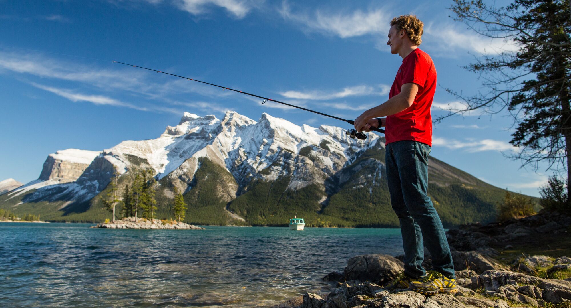 Man fishing from the shore in Lake Minnewanka witha view of the mountains in the background