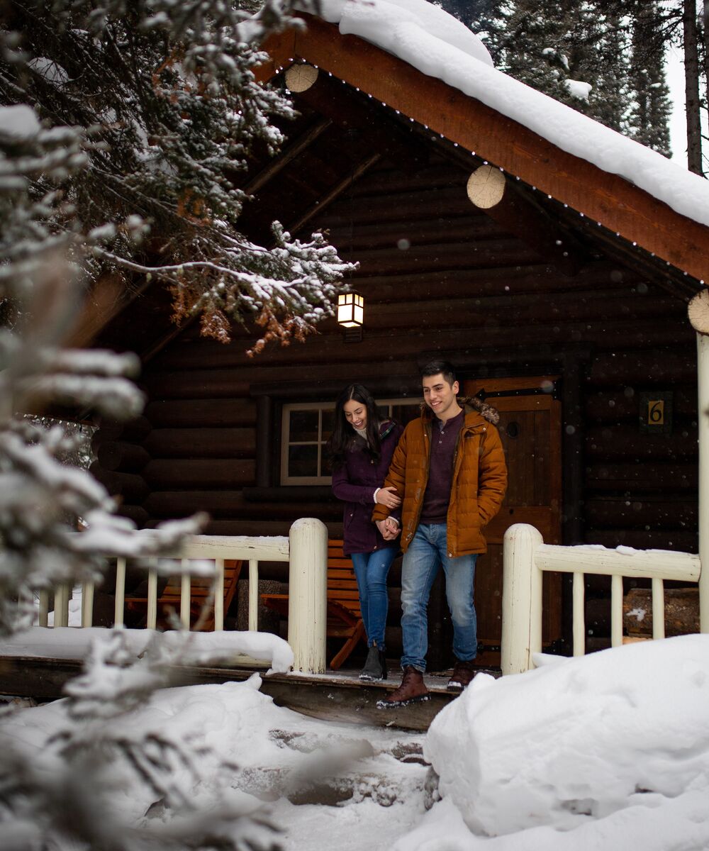 A cozy cabin in the woods in Banff National Park in the winter with snow falling.