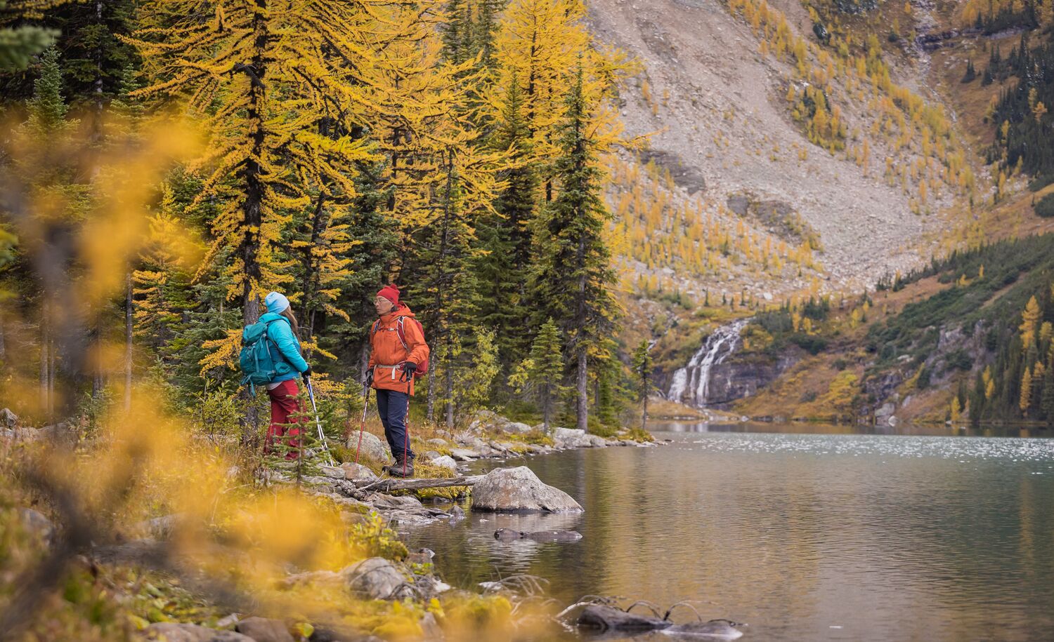 Two people stand on the edge of Taylor Lake in Banff National Park during larch season.
