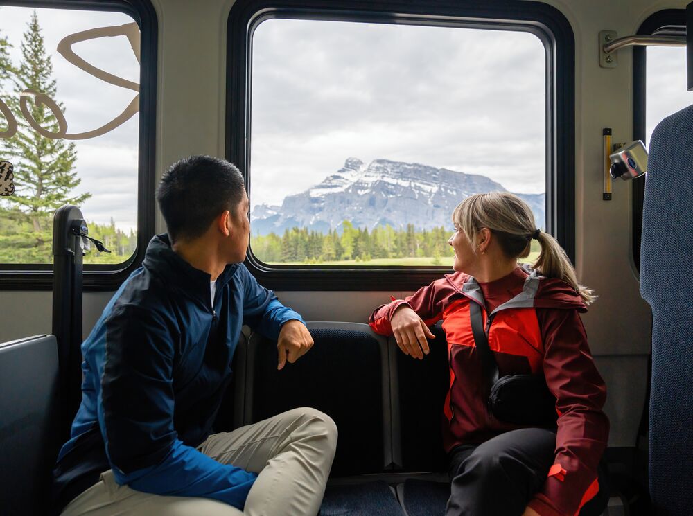 Two people look out a Roam Transit bus window at Mount Rundle while riding on the Minnewanka Loop.