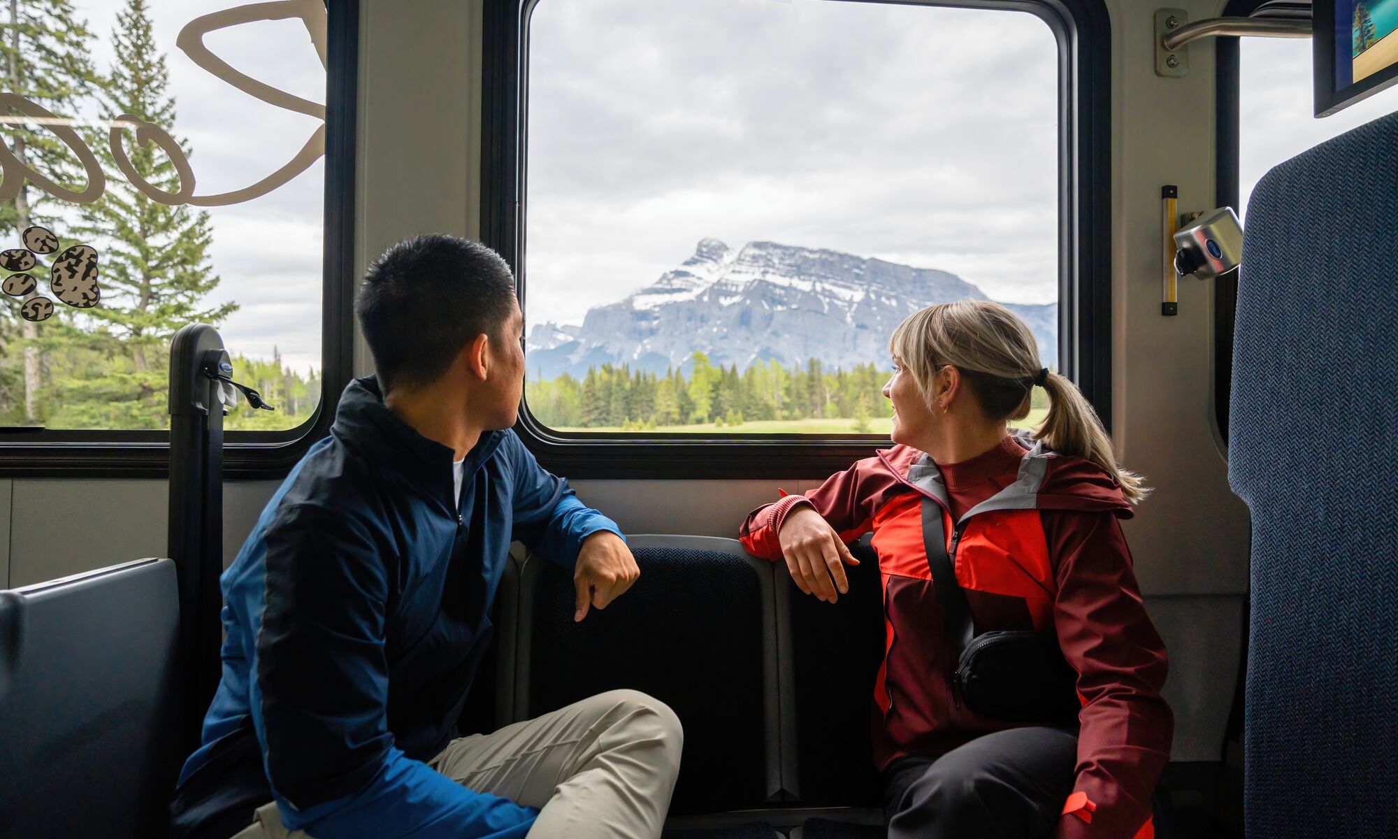 Two people look out a Roam Transit bus window at Mount Rundle while riding on the Minnewanka Loop.