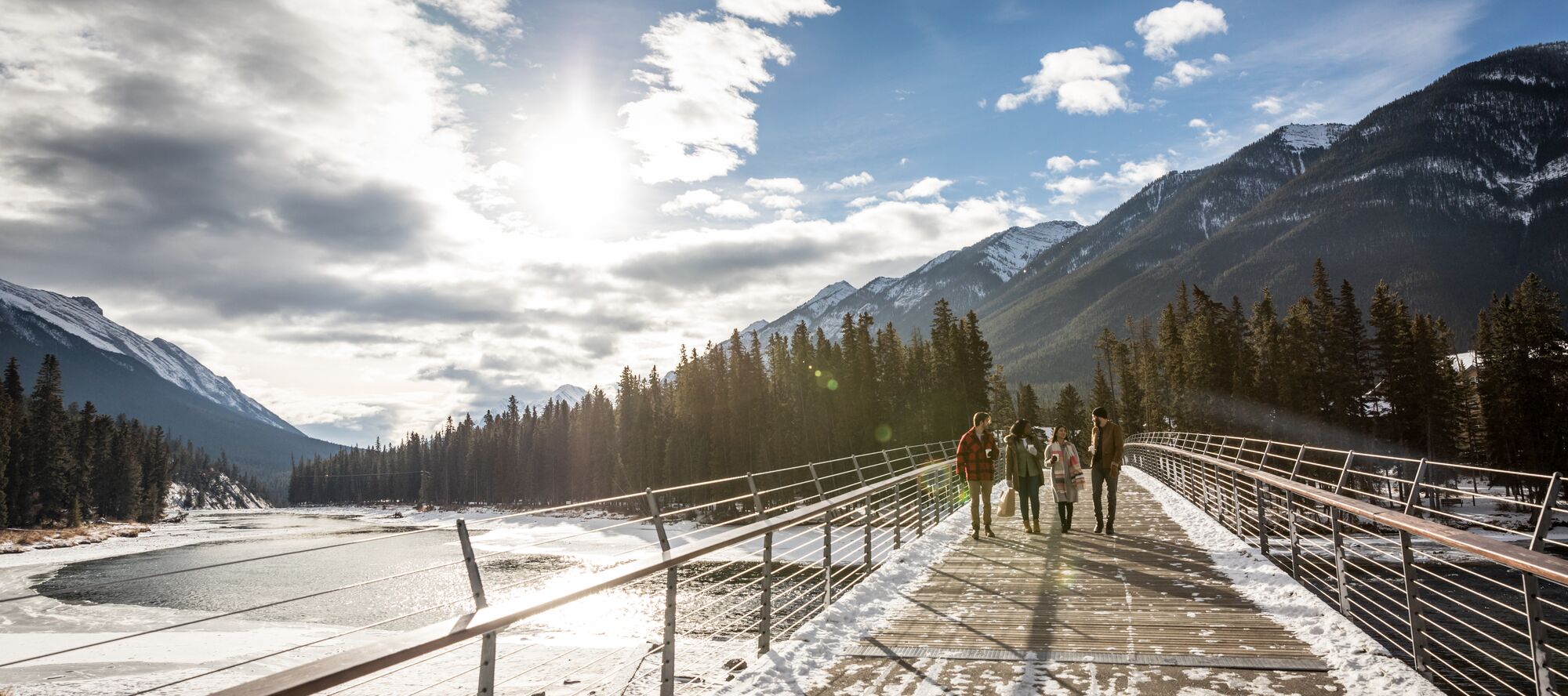 Four friends walk across the Banff Pedestrian Bridge over Bow River in Banff National Park